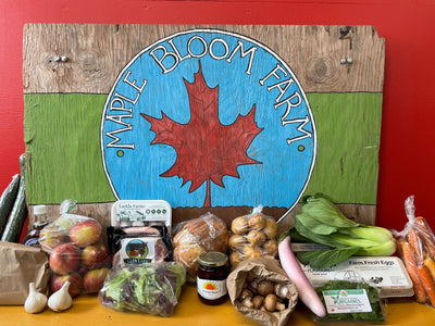 Maple Bloom Farm sign with variety of fresh fruits, vegetables, and other local produce arranged in front